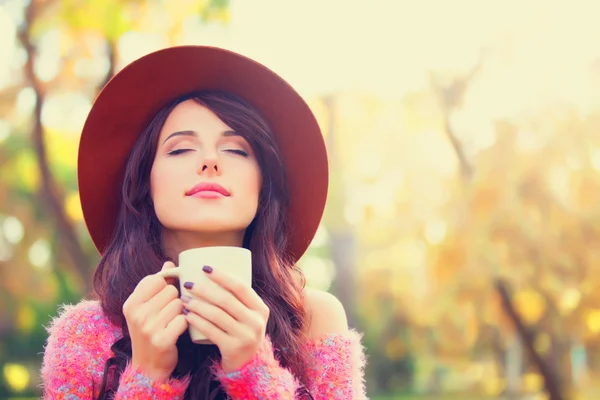 Brunette meisje met kop koffie in de herfst park. — Stockfoto