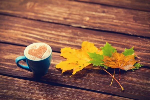 Jesienią liście oraz filiżanka kawa na drewnianym stole. — Zdjęcie stockowe