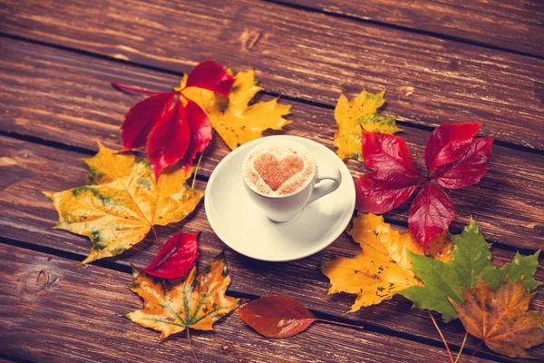 Herfst bladeren en koffie cup op houten tafel. — Stockfoto