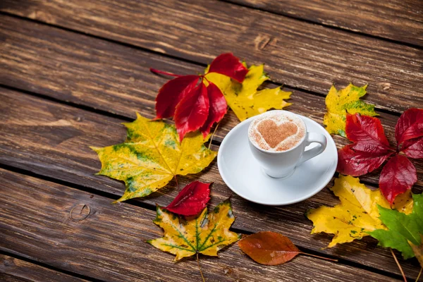 Sonbahar yaprakları ve ahşap masa fincan kahve. — Stok fotoğraf