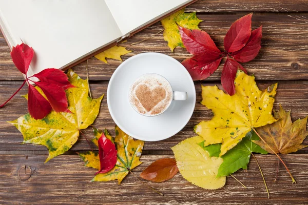 Foglie autunnali, libro e tazza di caffè sul tavolo di legno . — Foto Stock