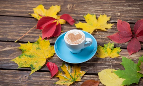 Hojas de otoño y taza de café sobre mesa de madera . — Foto de Stock