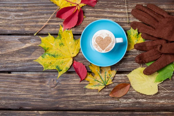 Foglie autunnali, guanti e tazzina da caffè sul tavolo di legno . — Foto Stock