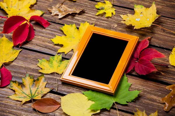 Hojas de otoño y marco para foto en mesa de madera . — Foto de Stock