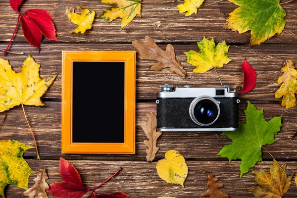 Autumn leafs, camera and frame on wooden table. — Stock Photo, Image