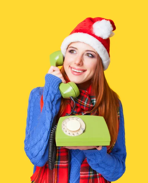 Beautiful redhead girl in christmas hat with telephone on yellow — Stock Photo, Image