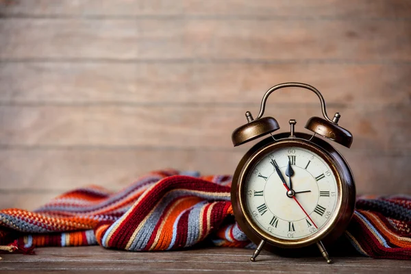 Reloj despertador retro y bufanda en mesa de madera . — Foto de Stock