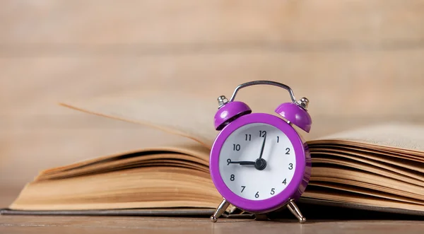 Relógio de alarme e livro aberto em uma mesa . — Fotografia de Stock