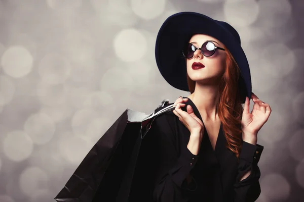 Stijl roodharige meisje met zonnebril en shopping tassen. — Stockfoto