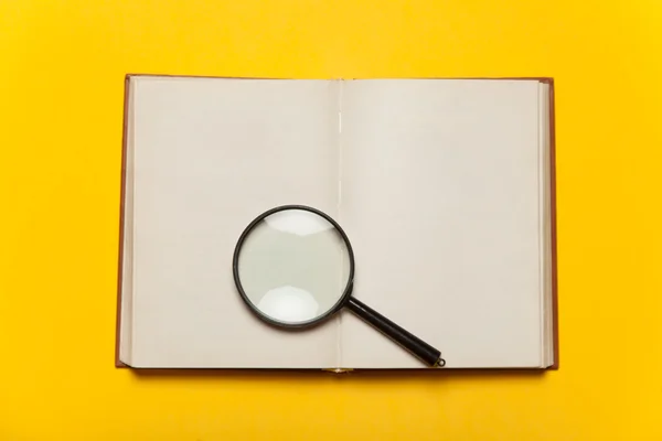 Opened book and loupe on color background. — Stock Photo, Image