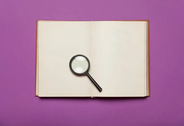 Buch und Lupe geöffnet auf farbigem Hintergrund. — Stockfoto