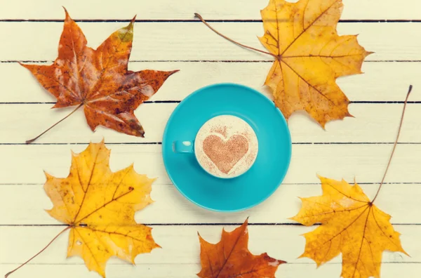 Taza de café y hojas de arce sobre mesa de madera . — Foto de Stock