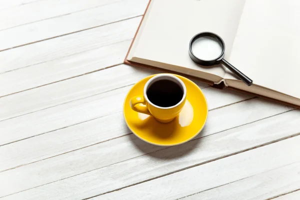 Kopje koffie en boek met loep op houten tafel. — Stockfoto