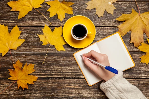 Mujer escribiendo algo a mano en un cuaderno cerca de una taza de café . —  Fotos de Stock