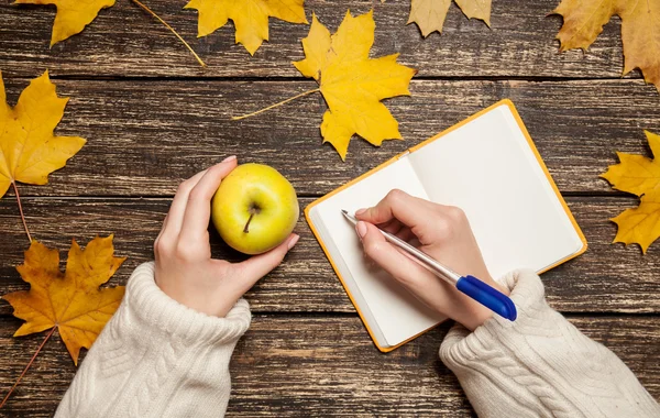 Mano femminile che scrive qualcosa sul quaderno e tiene in mano la mela — Foto Stock