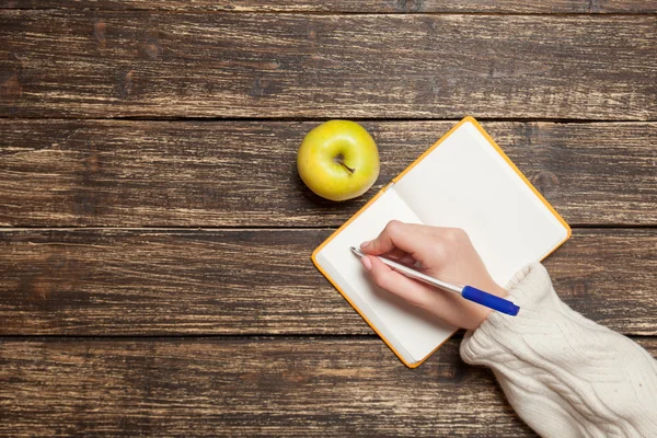 Kvinnlig hand skriva något i anteckningsboken nära apple — Stockfoto