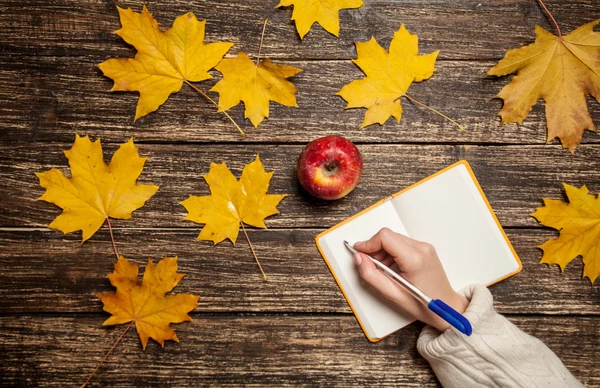 Female hand writing something in notebook next to apple — Stock Photo, Image