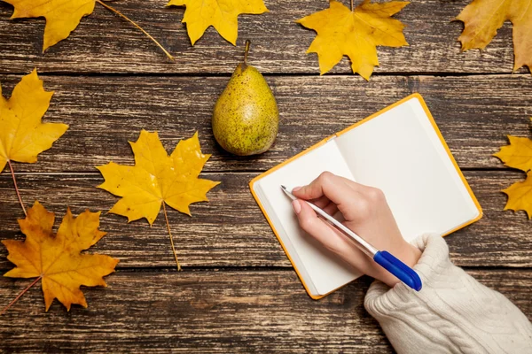 Weibliche Hand schreibt etwas in ein Notizbuch in der Nähe von Birne auf einem Tisch — Stockfoto