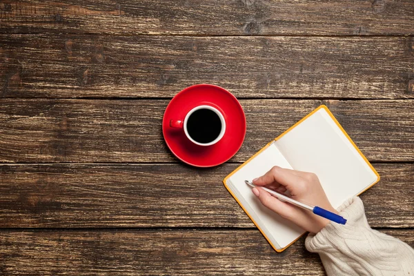 Mão feminina escrevendo algo no caderno perto de xícara de café . — Fotografia de Stock