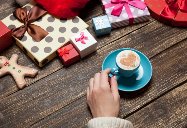 Gospodarstwo kobiece filiżankę kawy na drewnianym stole w pobliżu prezent na Boże Narodzenie — Zdjęcie stockowe