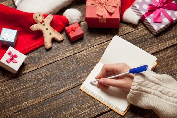 Female writing wish list in to notebook near christmas gifts — Stock Photo, Image