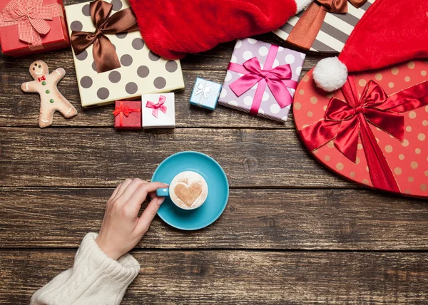 Female holding cup of coffee on wooden table near christmas gift — Stock Photo, Image