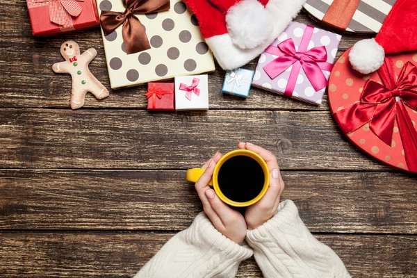 Kvinnliga anläggning kopp kaffe på träbord nära julklapp — Stockfoto