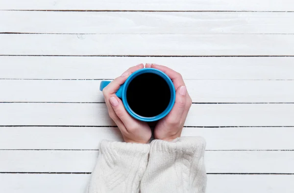 Kvinnliga händer som håller kopp kaffe på träbord. — Stockfoto