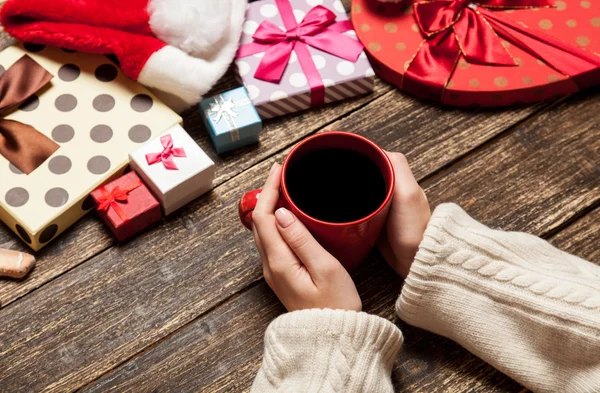 Kvinnliga anläggning kopp kaffe på träbord nära julklapp — Stockfoto