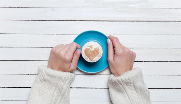 Manos femeninas sosteniendo la taza de café en la mesa de madera . — Foto de Stock