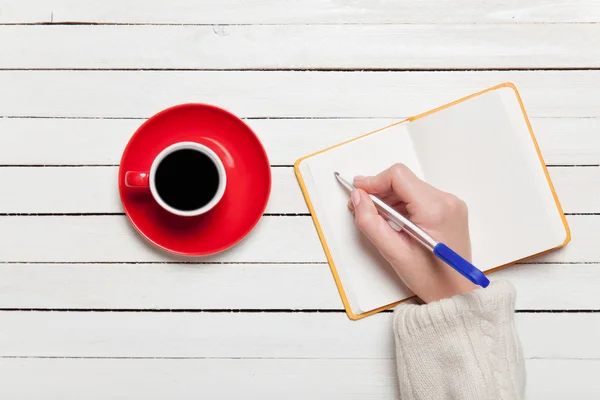 Mão feminina escrevendo algo no caderno perto de xícara de café . — Fotografia de Stock