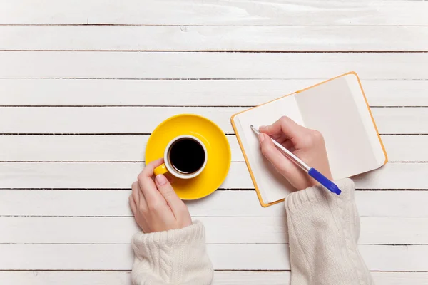 Mano femminile scrivere qualcosa nel taccuino vicino a tazza di caffè . — Foto Stock