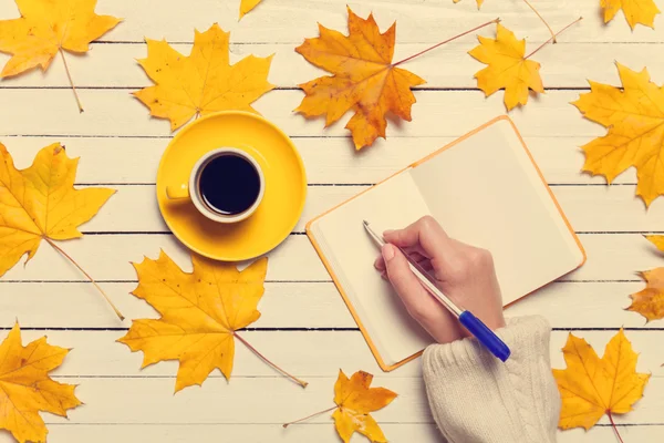 Mujer escribiendo algo a mano en un cuaderno cerca de una taza de café . — Foto de Stock