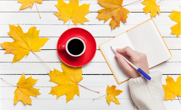 Mujer escribiendo algo a mano en un cuaderno cerca de una taza de café . — Foto de Stock