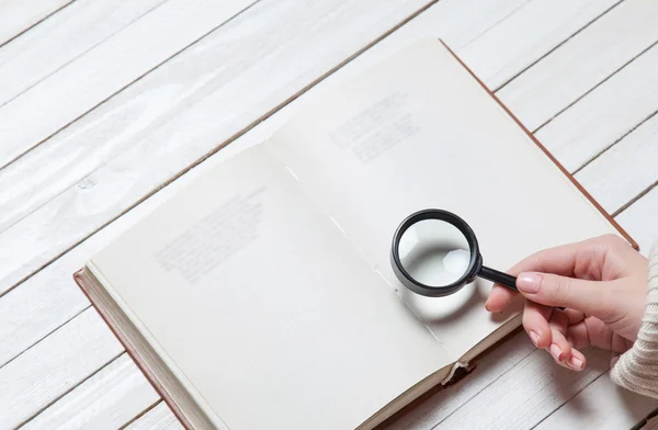 Female hand holding loupe over book — Stock Photo, Image