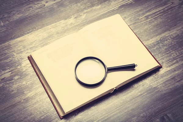 Book and loupe on wooden table. — Stock Photo, Image