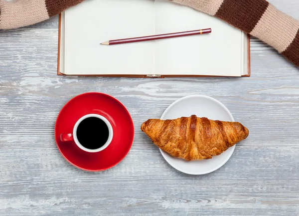 Cup, croissant en boek met sjaal op houten tafel. — Stockfoto