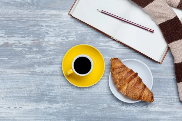 Copo, croissant e livro com cachecol na mesa de madeira . — Fotografia de Stock