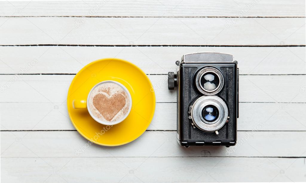 Retro camera and cup of coffee on wooden table.