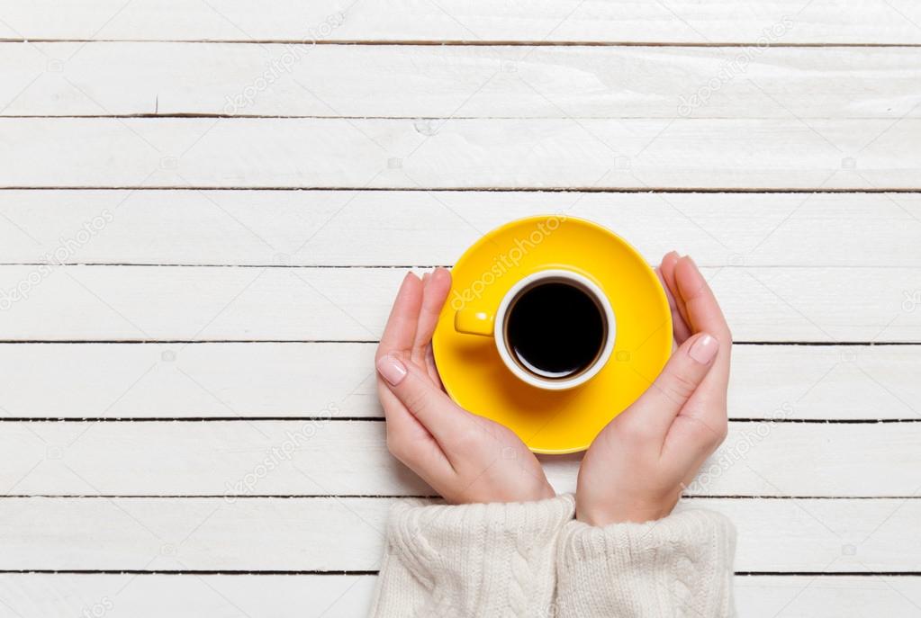 Female hands holding cup of coffee on wooden table.