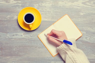 Female hand writing something in notebook near cup of coffee. clipart