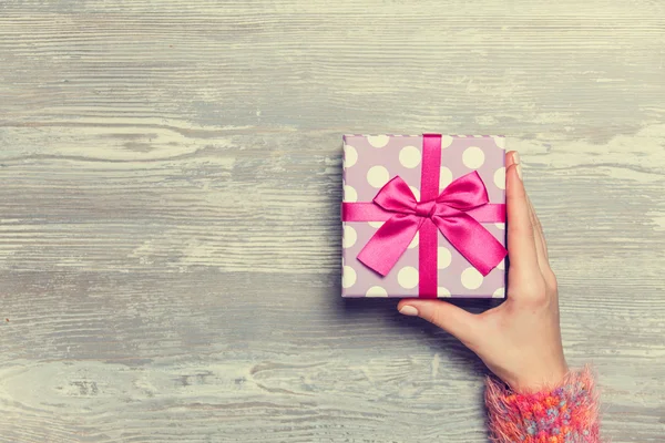 Female hands holding gift on wooden table. — Stock Photo, Image