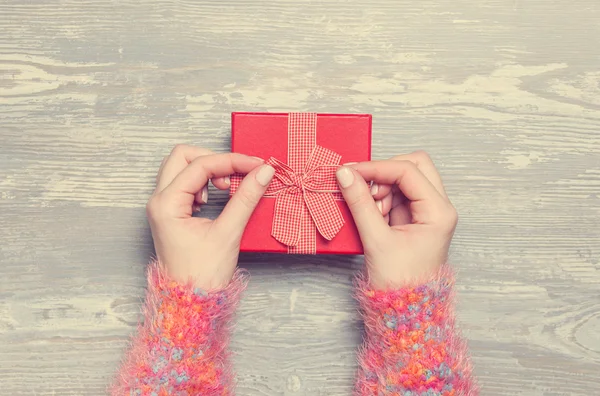 Manos femeninas sosteniendo regalo en mesa de madera. — Foto de Stock