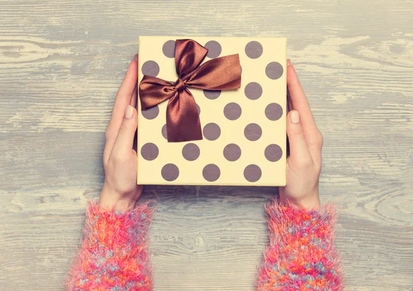 Manos femeninas sosteniendo regalo en mesa de madera. — Foto de Stock