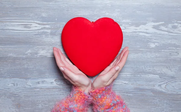 Vrouwelijke houden hart vorm speelgoed op een houten achtergrond. — Stockfoto