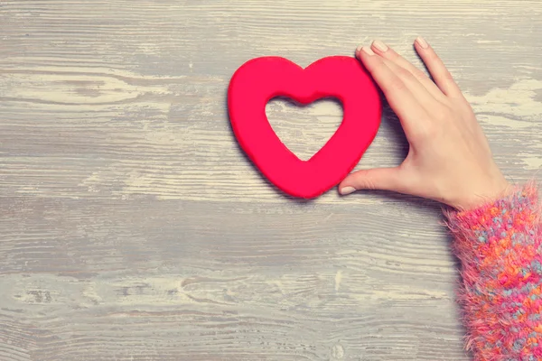 Vrouwelijke houden hart vorm speelgoed op een houten achtergrond. — Stockfoto