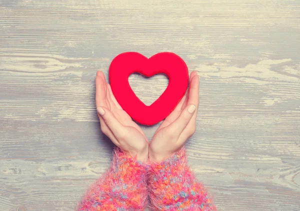 Vrouwelijke houden hart vorm speelgoed op een houten achtergrond. — Stockfoto