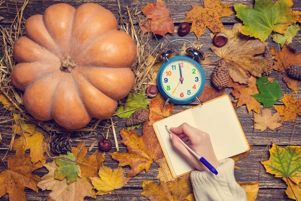 Vrouwelijke hand schrijven iets in notitieblok op herfst achtergrond. — Stockfoto