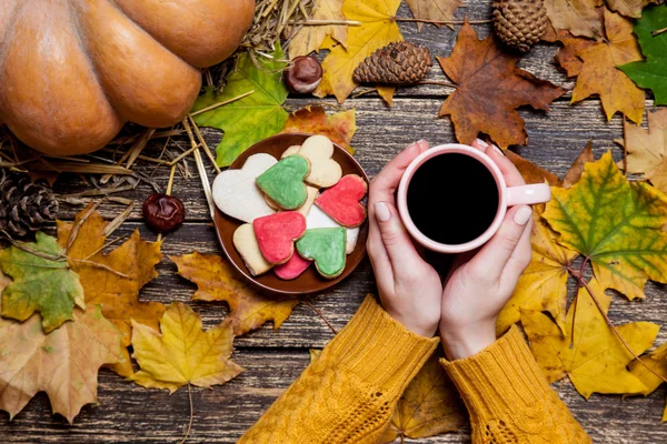 Weibchen halten Tasse Kaffee in der Nähe von Keksen auf herbstlichem Hintergrund. — Stockfoto