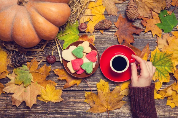 Weibchen halten Tasse Kaffee in der Nähe von Keksen auf herbstlichem Hintergrund. — Stockfoto